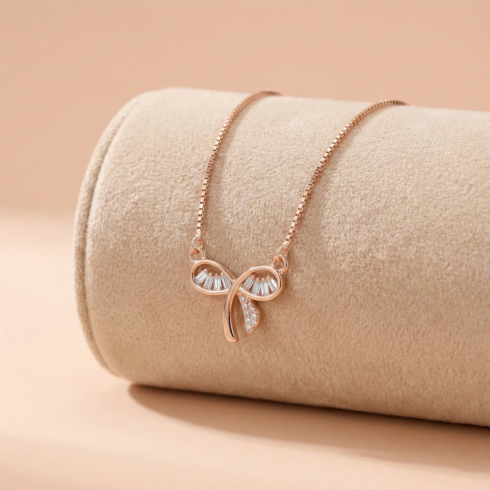 Rose gold necklace with bow pendant on a beige surface